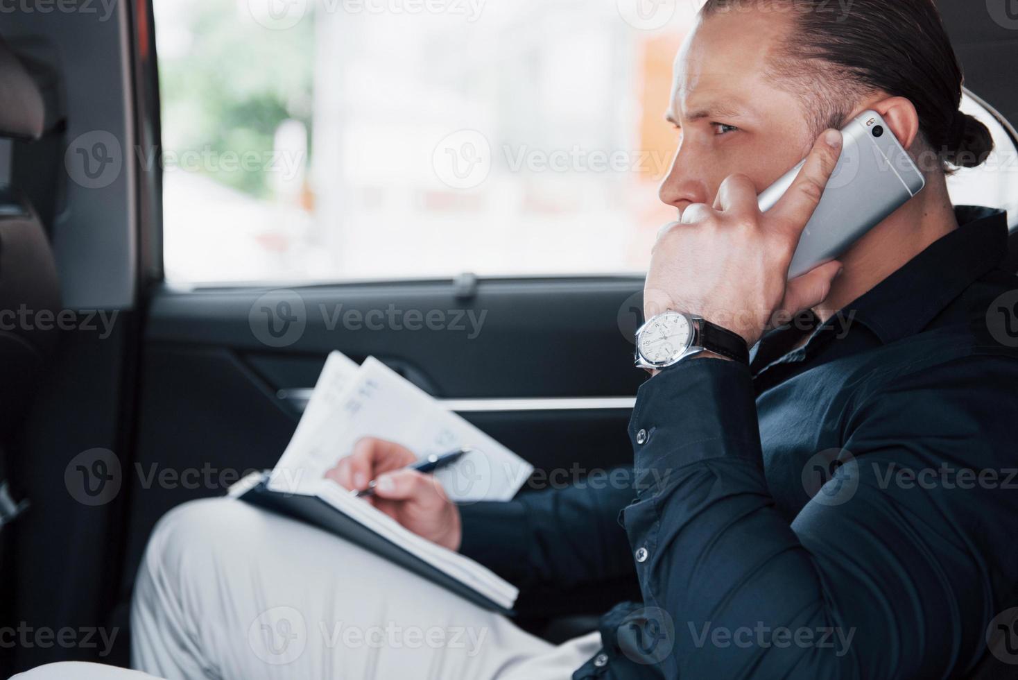 een jonge zakenman regelt zijn zaken met een notitieblok terwijl hij achter in de auto zit foto