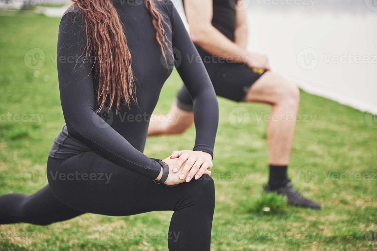 fitness paar die zich uitstrekt buiten in het park in de buurt van het water. jonge, bebaarde man en vrouw die 's ochtends samen trainen foto