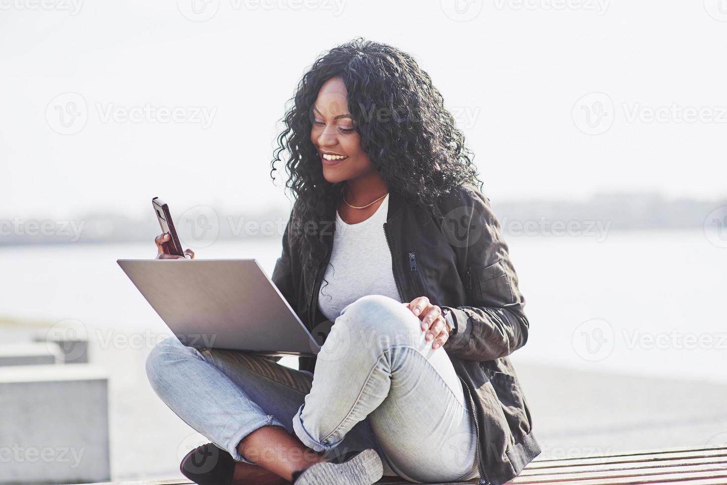 jonge vrouw op straat die aan laptop werkt en op mobiele telefoon praat foto