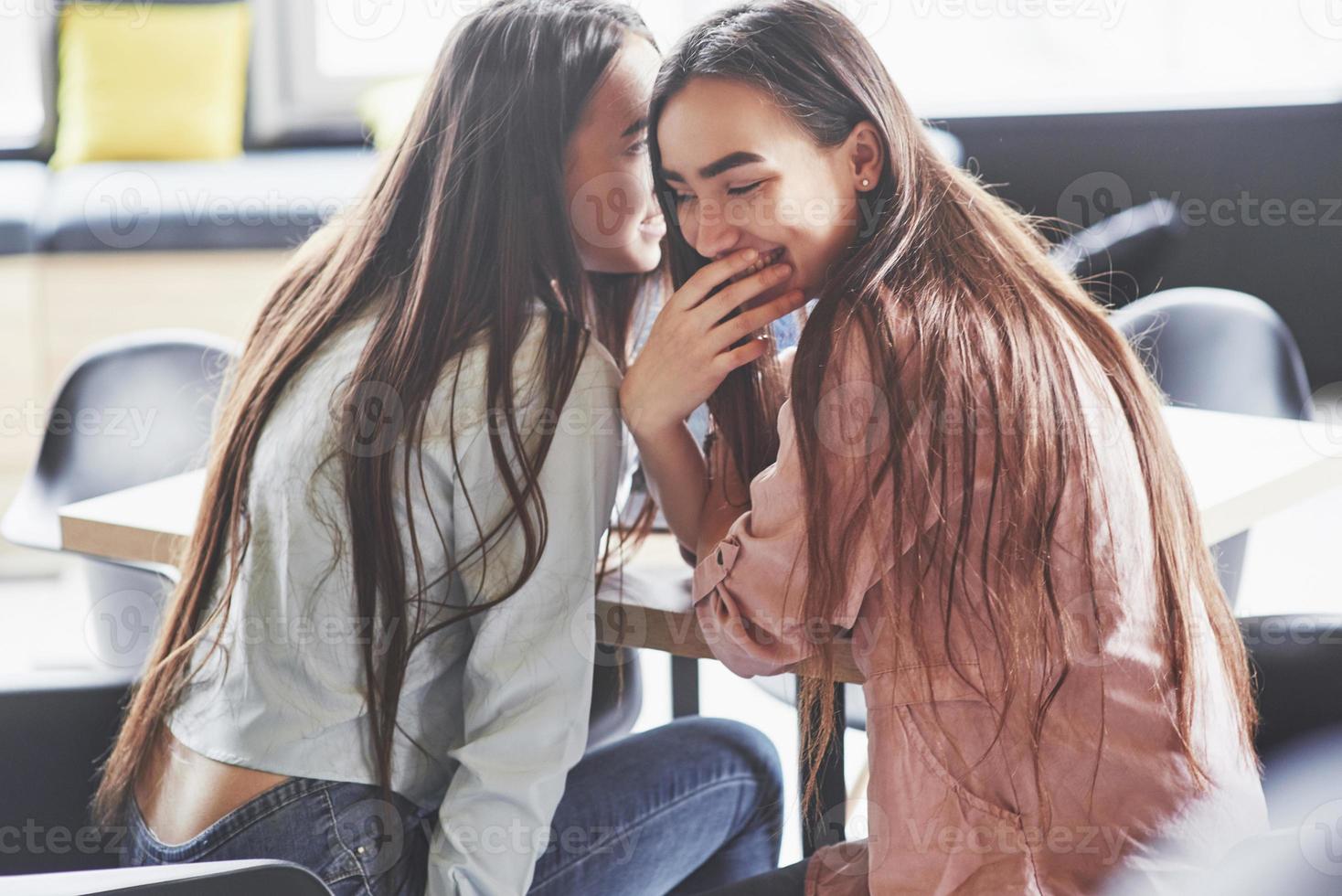 twee mooie tweelingmeisjes brengen tijd door. zussen ontspannen in een café en samen plezier maken en fluisteren foto