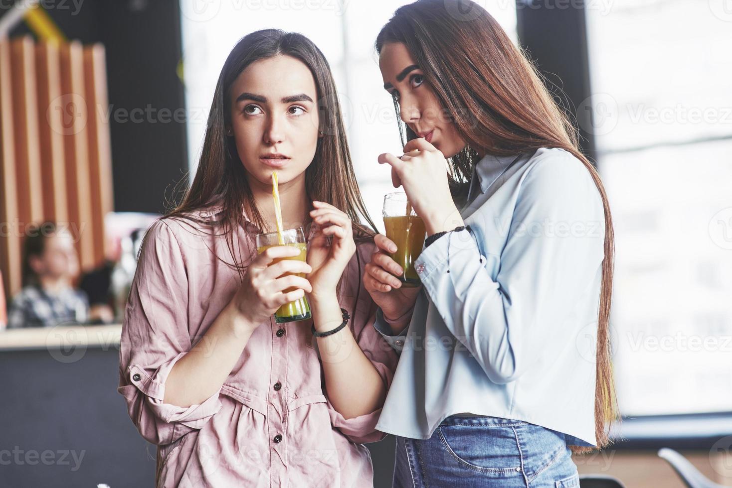 twee mooie tweelingmeisjes brengen tijd door met het drinken van sap. zussen ontspannen in een café en samen plezier maken en fluisteren foto