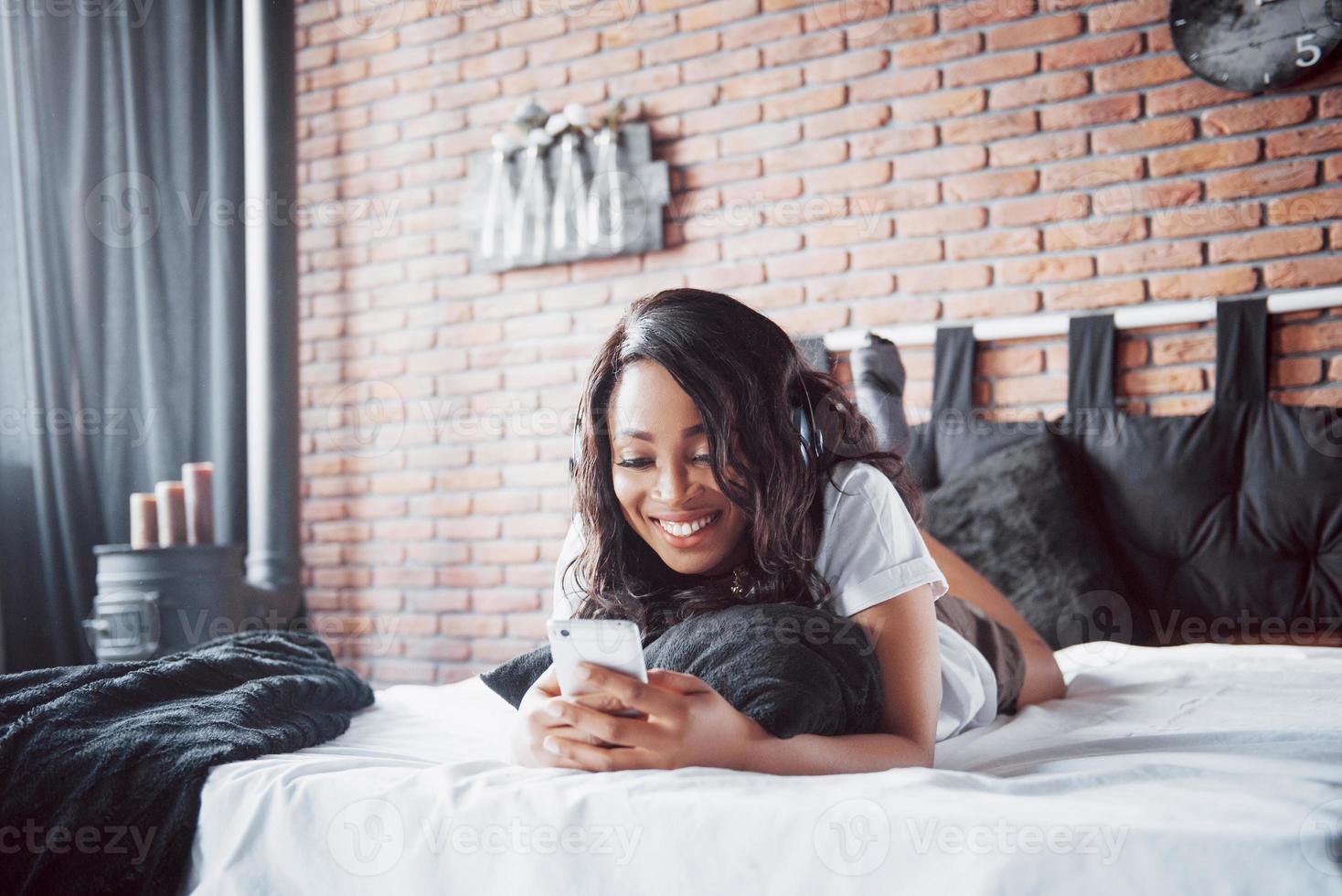 portret van mooie vrouw wakker in haar bed en kijkt in de telefoon. controleer sociale netwerken, stuur sms. het meisje draagt een t-shirt foto