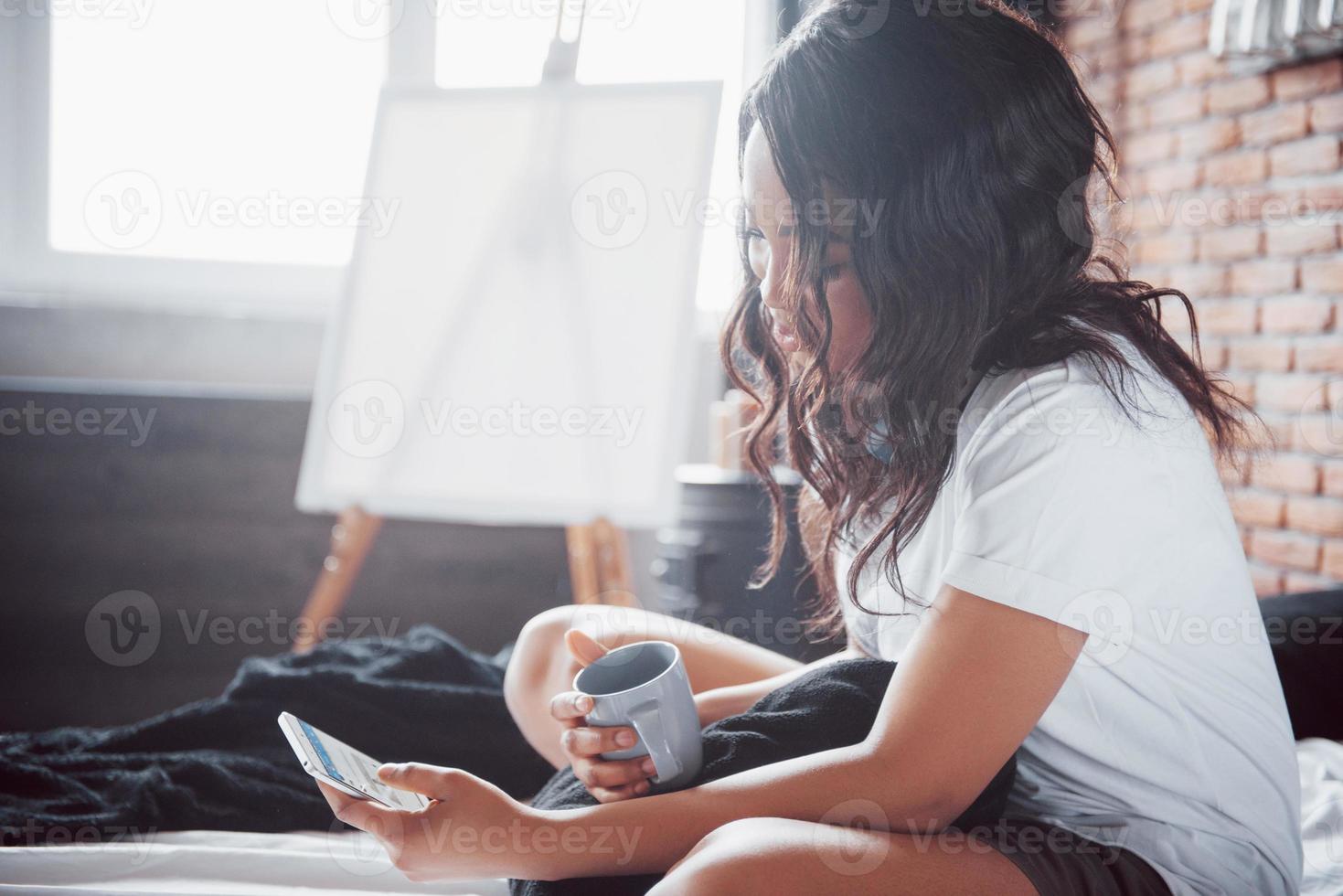 gelukkig mooi Afrikaans meisje in nachtkleding die zich uitstrekt glimlachend zittend op bed thuis werd 's ochtends wakker op een zonnige dag foto