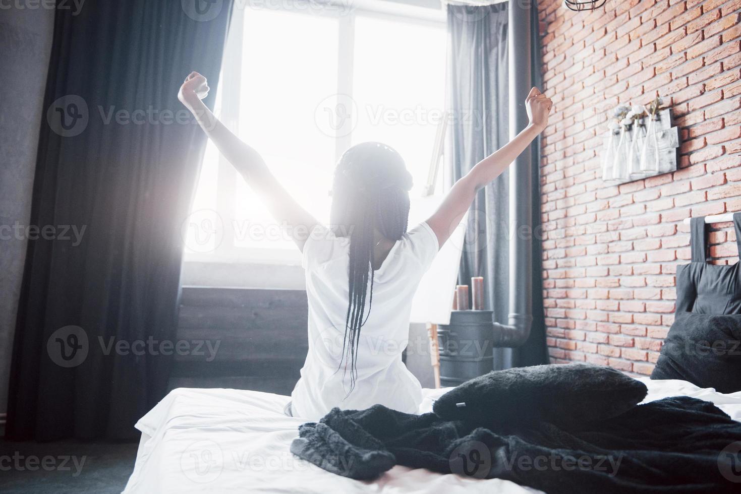 mooie zwarte vrouw die wakker wordt in haar bed, ze lacht en strekt zich uit foto