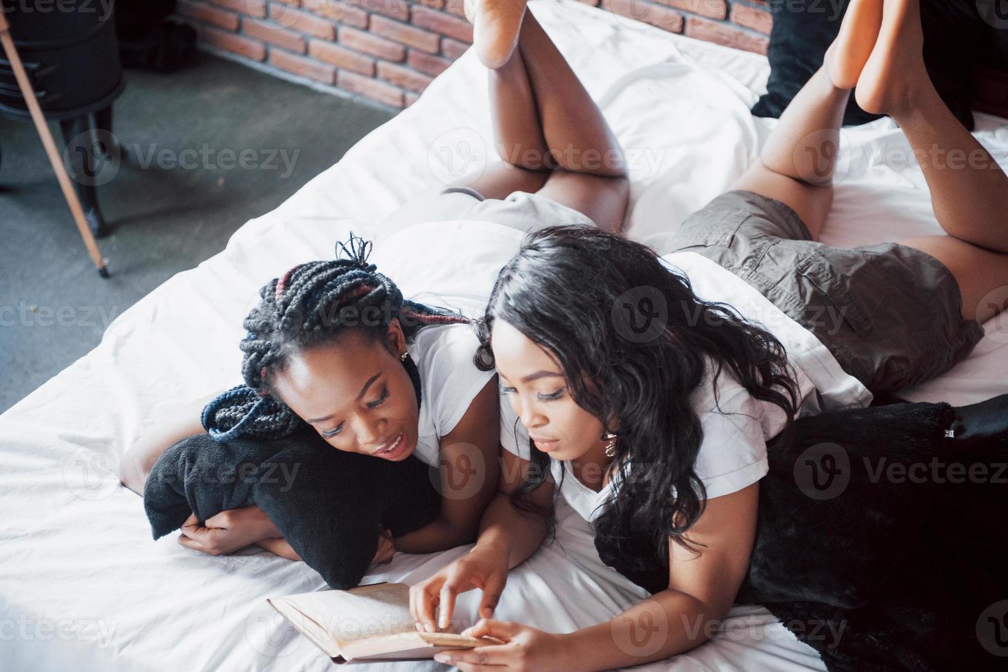 twee mooie Afrikaanse meisje in nachtkleding glimlachend zittend op bed thuis wakker in de ochtend op een zonnige dag. foto