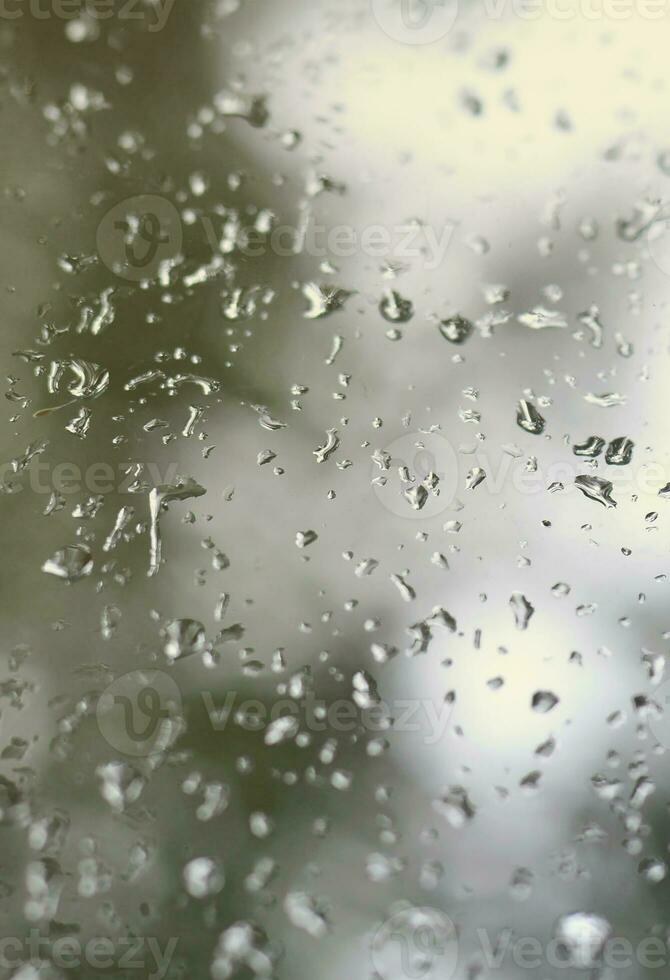 een foto van regen druppels Aan de venster glas met een wazig visie van de bloeiende groen bomen. abstract beeld tonen bewolkt en regenachtig weer voorwaarden