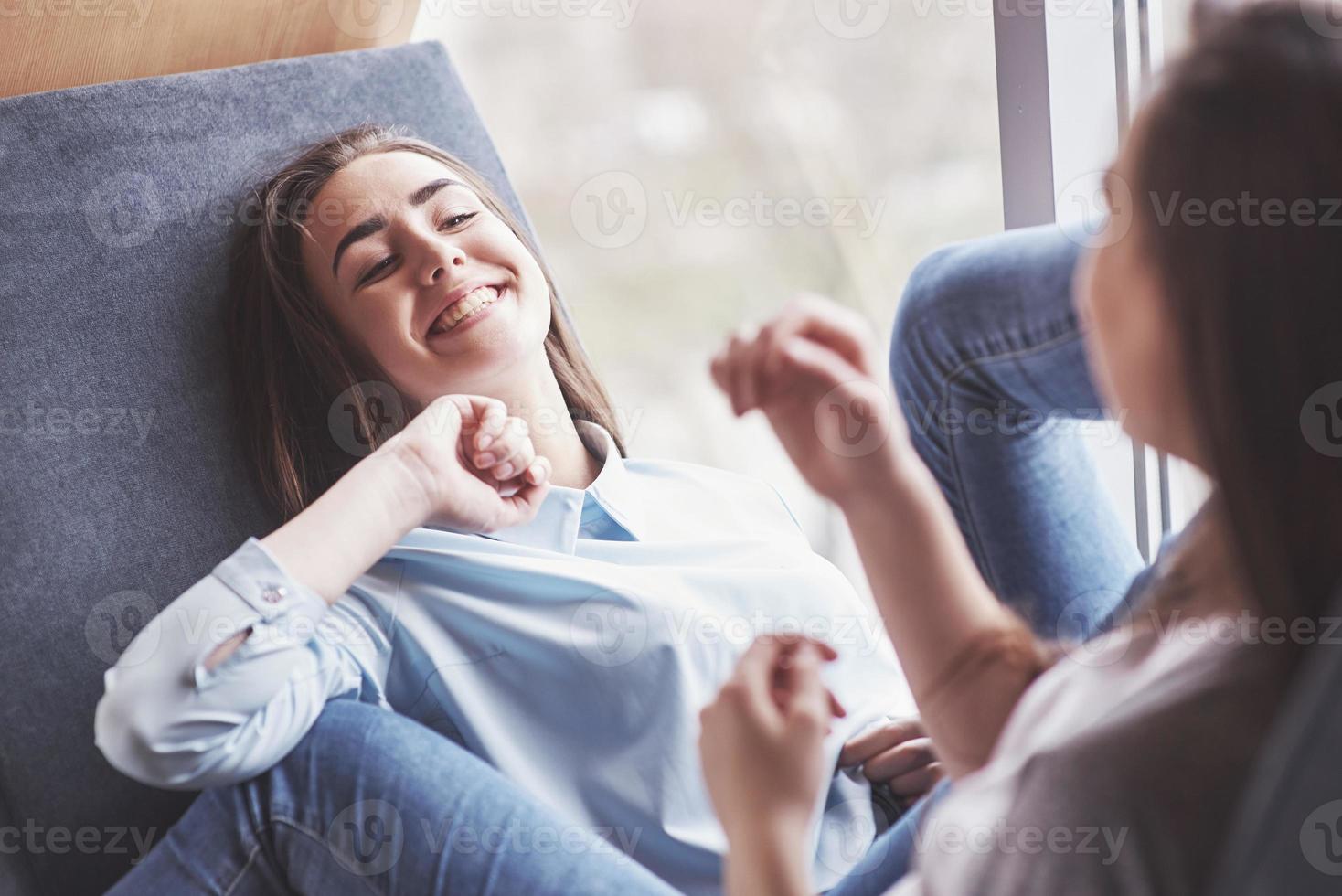 twee tweelingmeisjes zitten voor hen in een strakke fauteuil in de recreatieruimte. zussen poseren en plezier hebben tijd doorbrengen. doe altijd mee aan vriendschap en jeugdconcept foto