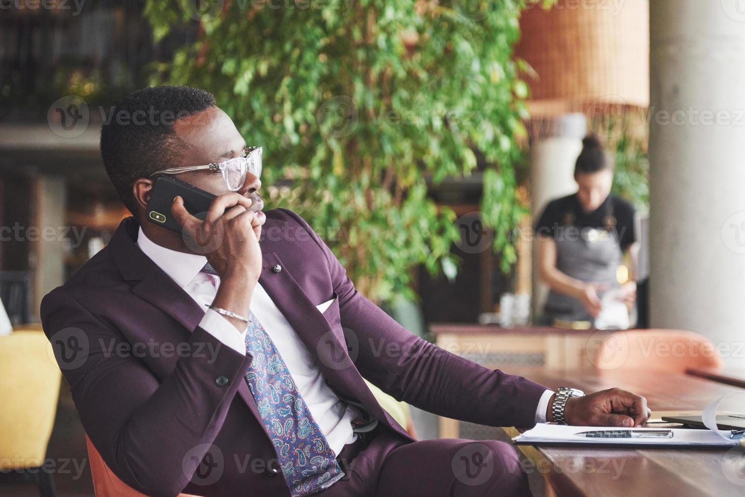 portret van een jonge en knappe Afro-Amerikaanse zakenman die in een pak aan de telefoon praat. voorbereiding van een zakelijke bijeenkomst. foto