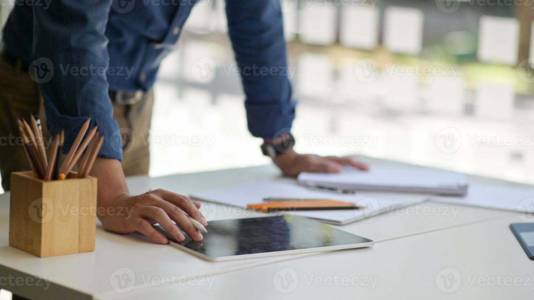 jonge man met een pen om een tablet te gebruiken op het bureau met briefpapier in een eigentijds kantoor. foto