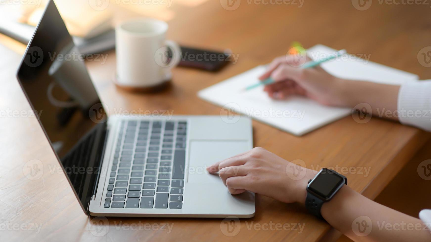 de hand van een jonge vrouw die een laptop gebruikt en een rapport schrijft, ze werkt vanuit huis. foto