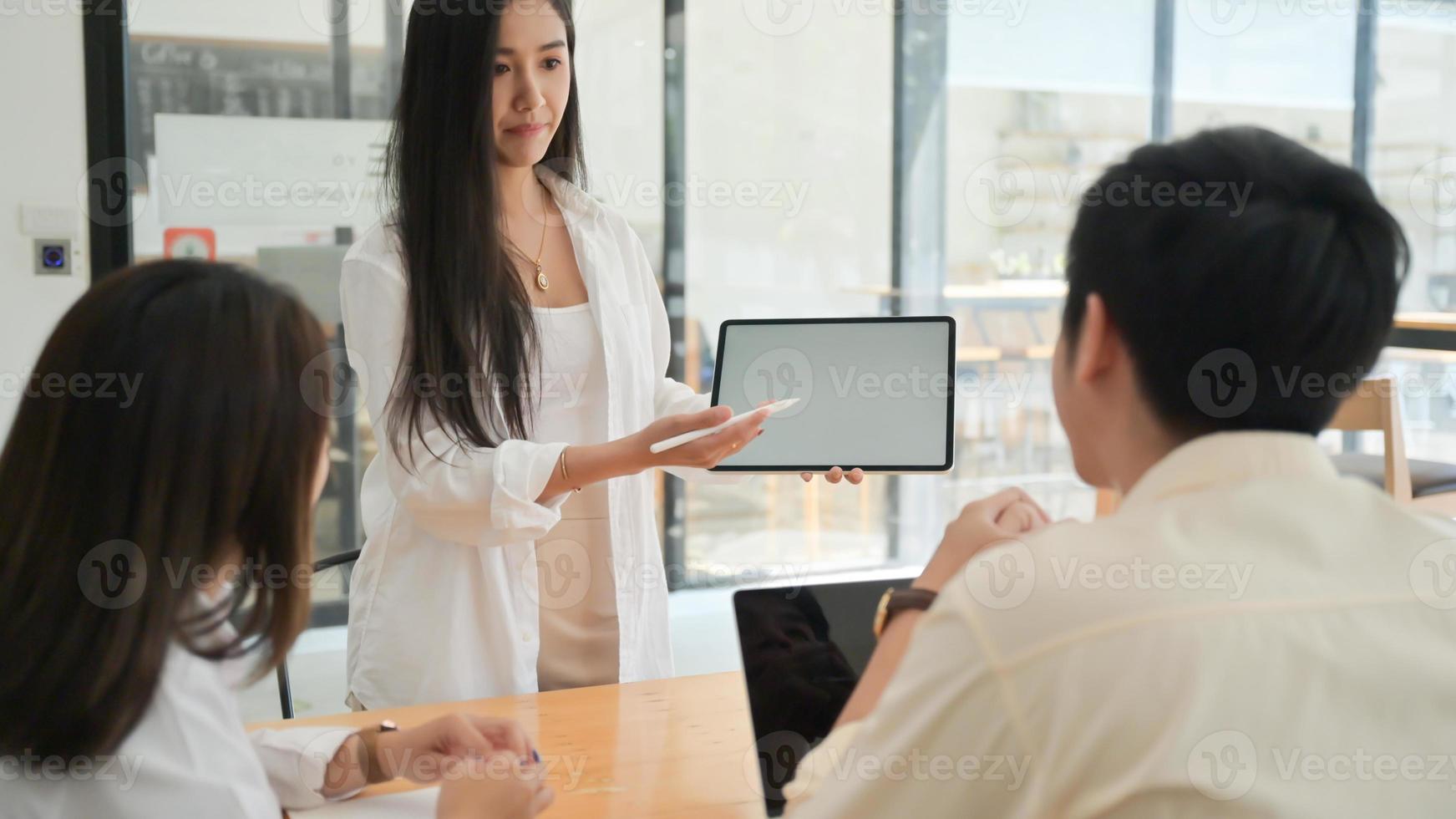 het team van jonge mannen en vrouwen presenteert een nieuw projectplan op tablet in een modern kantoor. foto