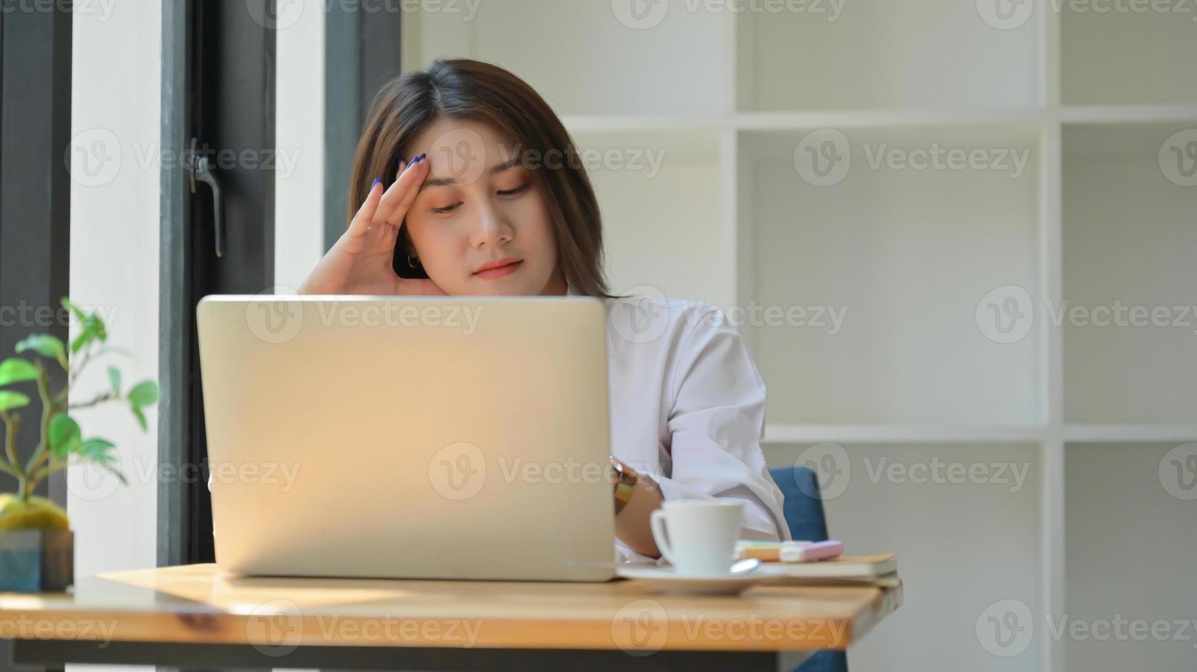 een jonge vrouw gebruikt een laptop voor haar werk, ze werkt thuis en is moe. foto