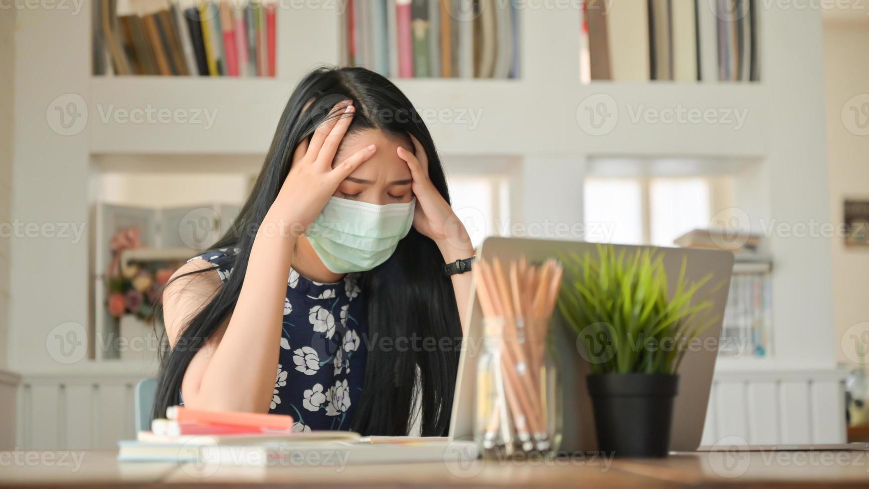 meisje dat een masker draagt en haar hoofd aanraakt, ze werkt thuis om te beschermen tegen het covid-19-virus. foto