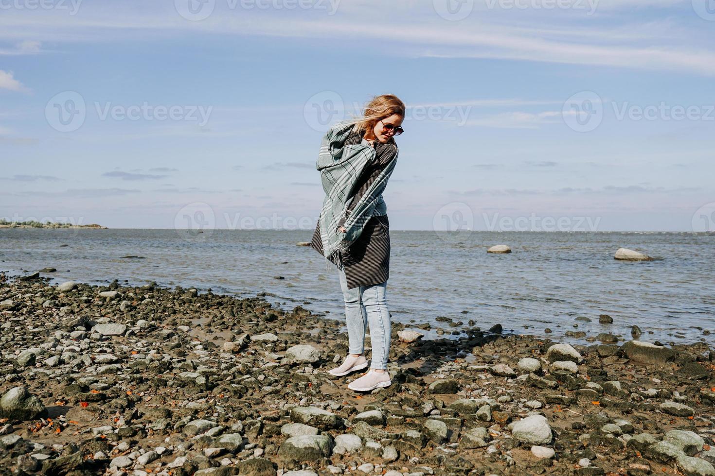 jonge vrouw in zonnebril gewikkeld in een sjaal, herfst aan de golf van finland foto