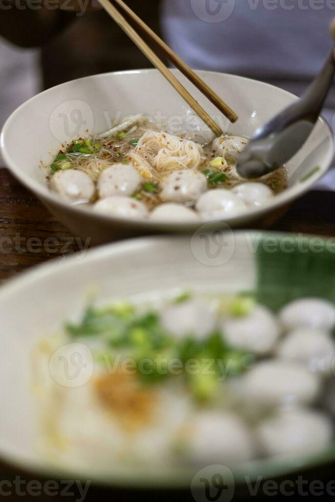 dichtbij omhoog van wit rijst- noedels, Doorzichtig soep, vlees ballen met ingrediënten in wit schaal. foto