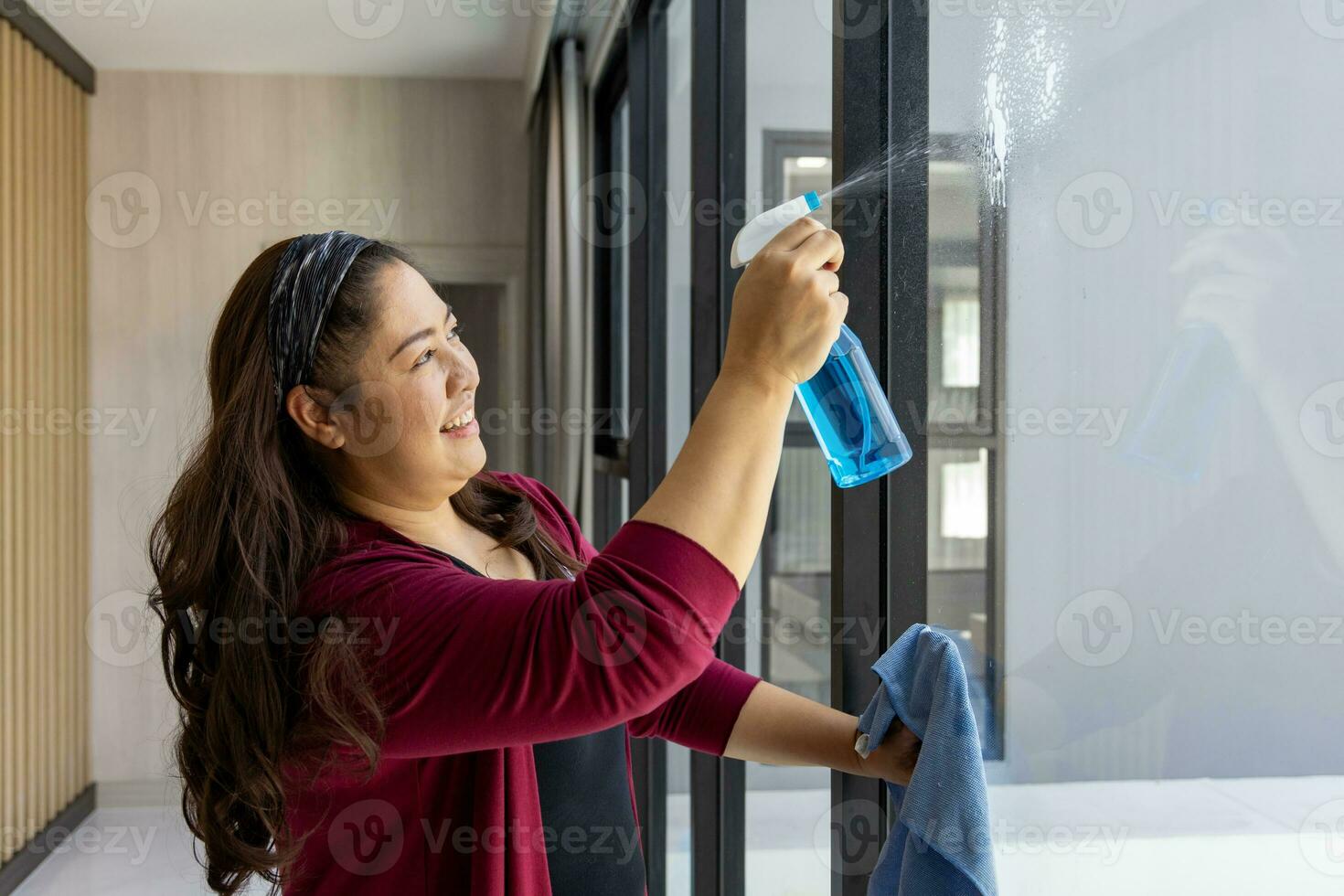 Aziatisch vrouw is schoonmaak de huis door afvegen de Doorzichtig glas venster voor dagelijks routine- klusjes en huishouding concept foto