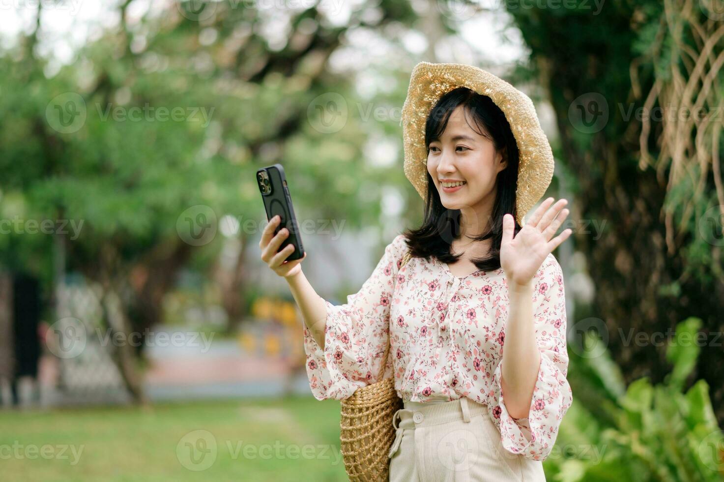portret van Aziatisch jong vrouw reiziger met het weven hoed en mand gebruik makend van mobiel telefoon Aan groen park natuur achtergrond. reis reis levensstijl, wereld reizen ontdekkingsreiziger of Azië zomer toerisme concept. foto