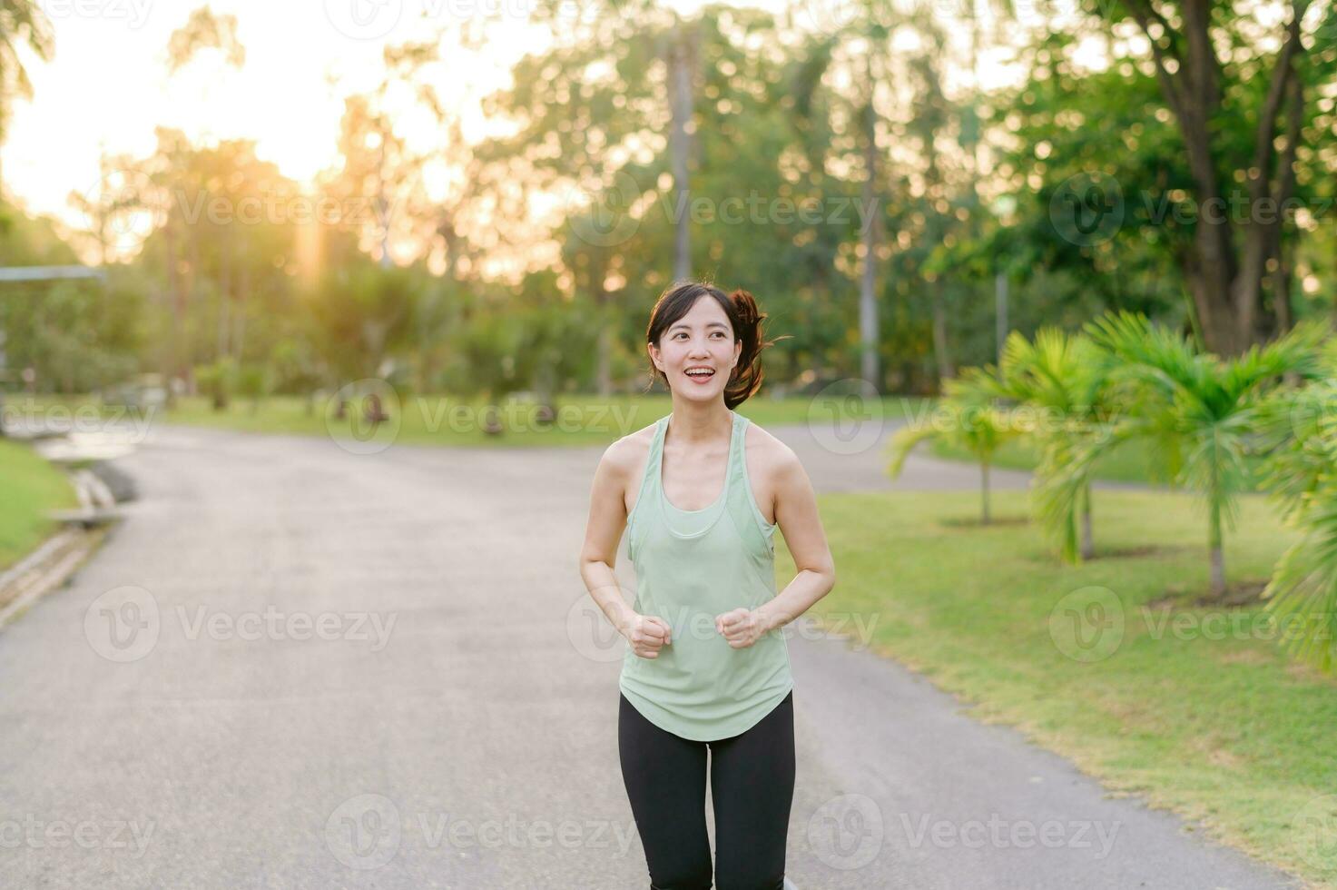 fit Aziatisch jong vrouw jogging in park glimlachen gelukkig rennen en genieten van een gezond buitenshuis levensstijl. vrouw jogger. geschiktheid loper meisje in openbaar park. gezond levensstijl en welzijn wezen concept foto