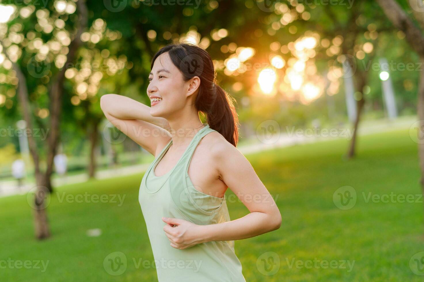 vrouw jogger. fit jong Aziatisch vrouw met groen sportkleding uitrekken spier in park voordat rennen en genieten van een gezond buitenshuis. geschiktheid loper meisje in openbaar park. welzijn wezen concept foto