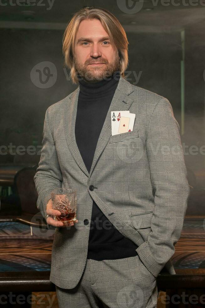 zelfverzekerd poker speler met twee azen in jasje zak- Holding glas van whisky in casino foto