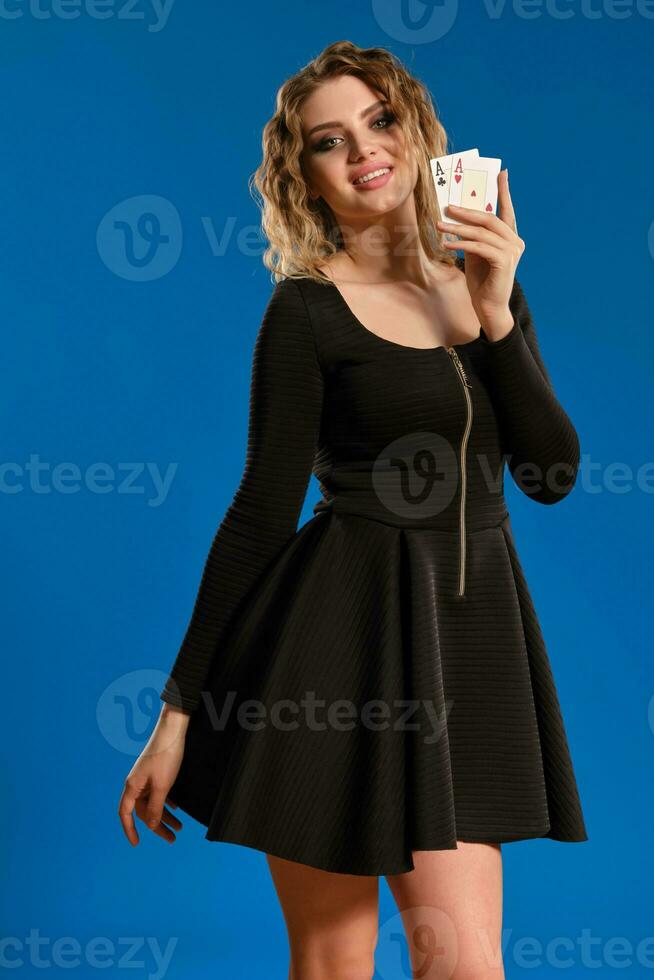 blond dame in zwart kort jurk is lachend, tonen twee spelen kaarten, poseren Aan blauw achtergrond. het gokken amusement, poker, casino. detailopname. foto