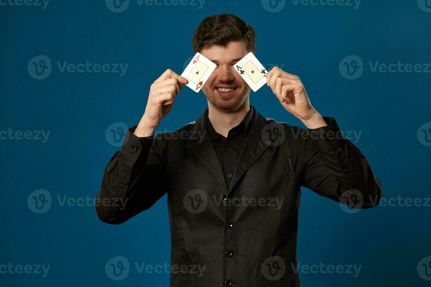 Nieuweling in poker, in zwart hesje en shirt. Holding twee spelen kaarten terwijl poseren tegen blauw studio achtergrond. gokken, casino. detailopname. foto