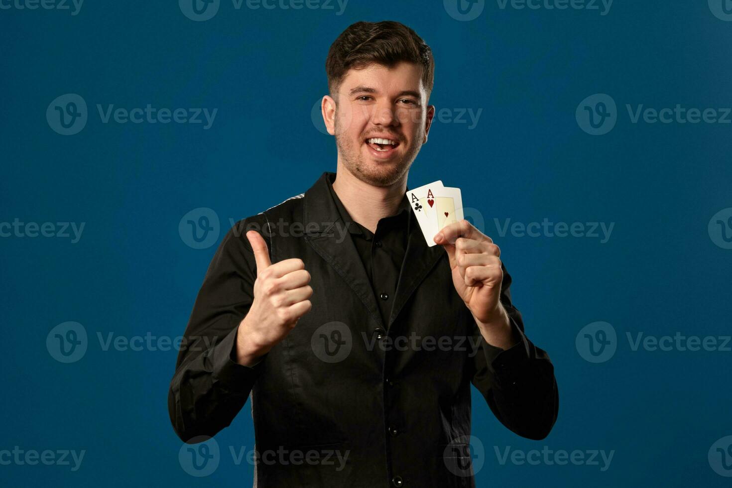 nieuweling in poker, in zwart hesje en shirt. Holding twee spelen kaarten terwijl poseren tegen blauw studio achtergrond. gokken, casino. detailopname. foto