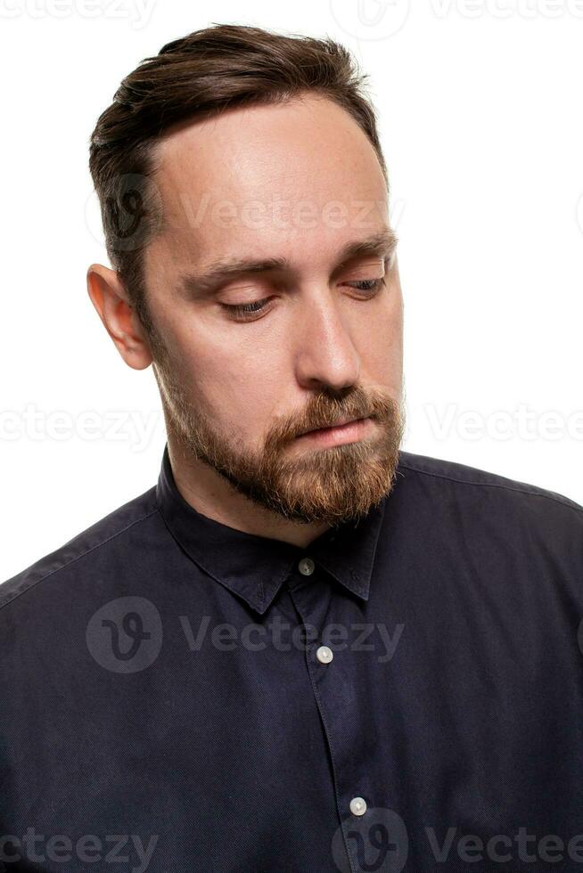 portret van een knap, ongeschoren Mens, gekleed in een donker blauw shirt, staand tegen een wit achtergrond. zelf zelfverzekerd Mens. foto