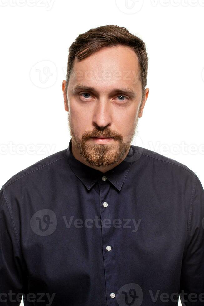 portret van een knap, ongeschoren Mens, gekleed in een donker blauw shirt, staand tegen een wit achtergrond. zelf zelfverzekerd Mens. foto