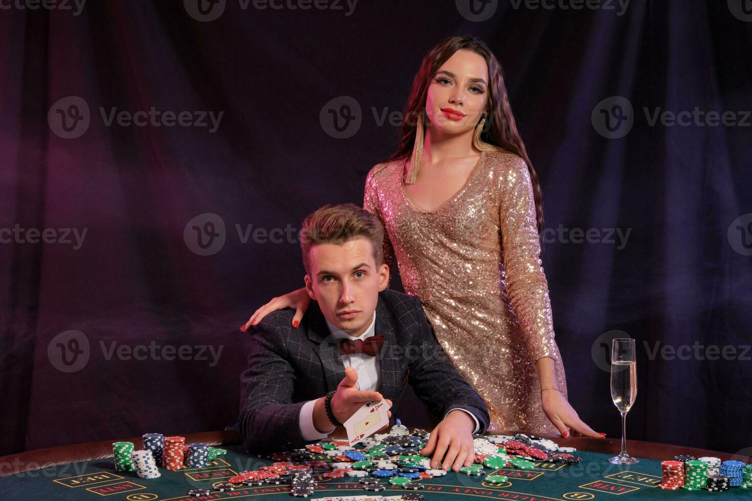 Mens spelen poker Bij casino zittend Bij tafel met stapels van chips, geld, Champagne, kaarten. vieren winnen met vrouw. zwart achtergrond. detailopname. foto