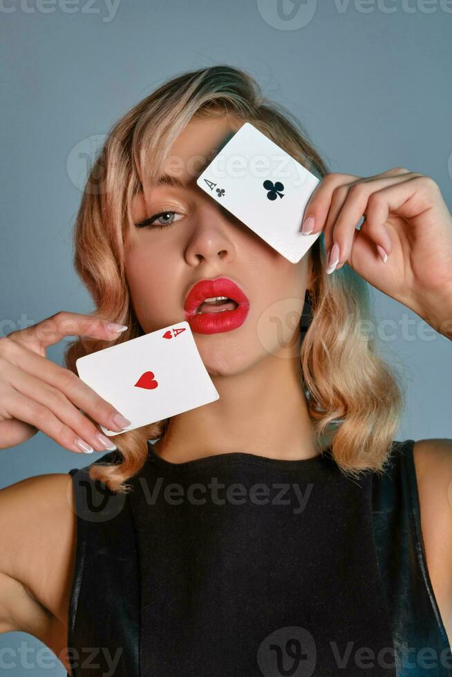 blond meisje in zwart leer jurk tonen twee spelen kaarten, poseren tegen grijs achtergrond. het gokken amusement, poker, casino. detailopname. foto