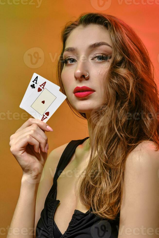 brunette vrouw met oorbel in neus, in zwart jurk. tonen twee azen, poseren Aan kleurrijk achtergrond. gokken, poker, casino. detailopname foto