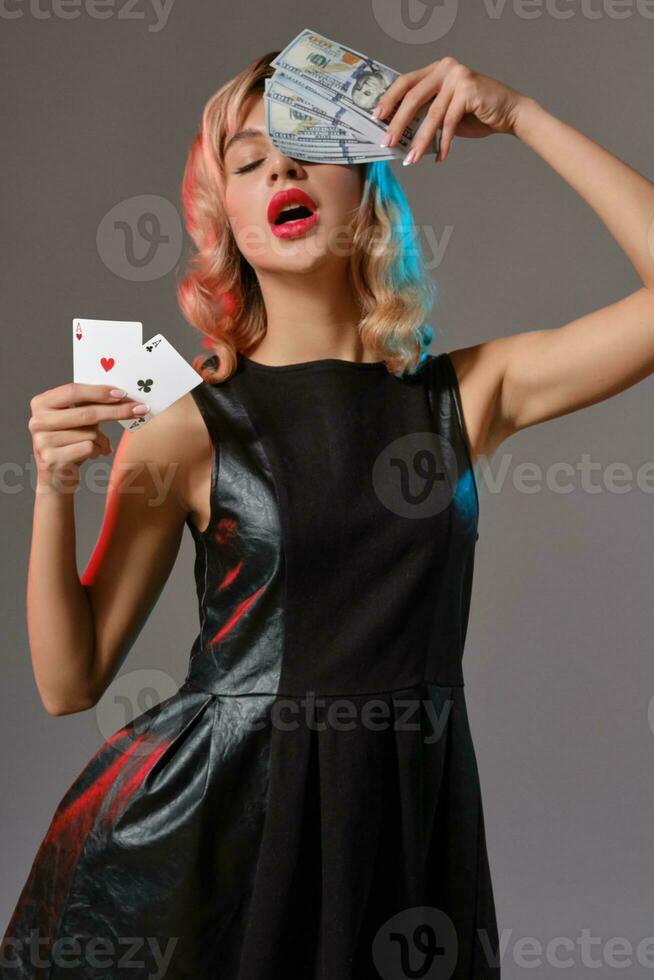 blond meisje in zwart elegant jurk Holding sommige geld en kaarten, poseren tegen grijs achtergrond. het gokken amusement, poker, casino. detailopname. foto