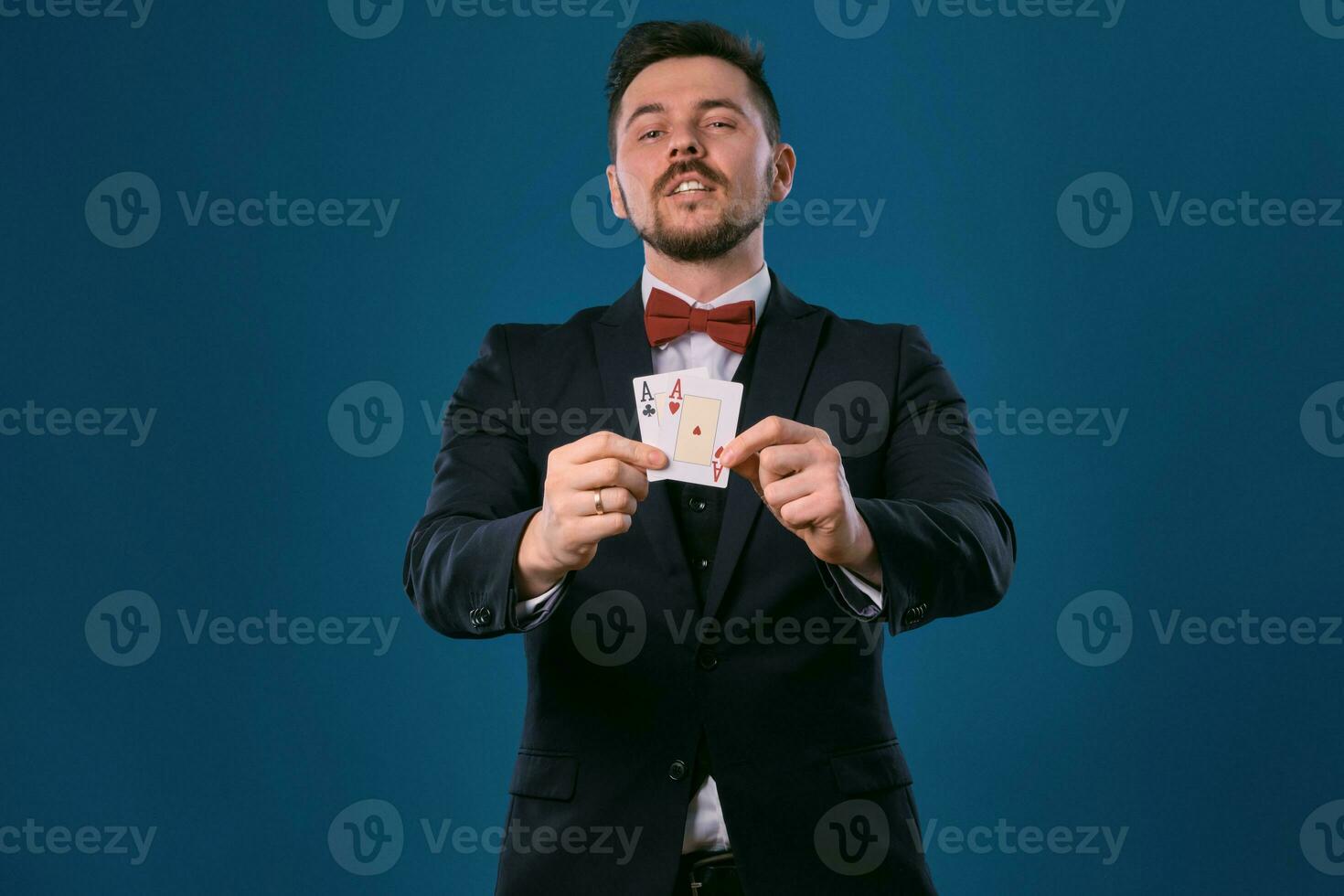 Mens in zwart klassiek pak en rood vlinderdas tonen twee spelen kaarten terwijl poseren tegen blauw studio achtergrond. gokken, poker, casino. detailopname. foto