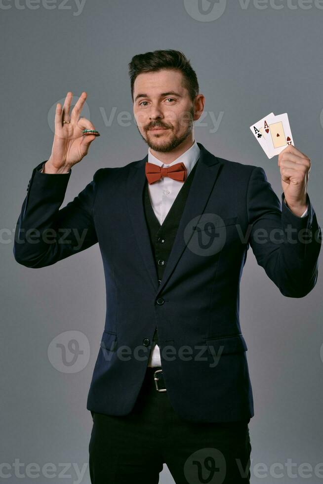 Mens in zwart klassiek pak en rood vlinderdas tonen twee spelen kaarten en chips, poseren Aan grijs studio achtergrond. gokken, poker, casino. detailopname. foto