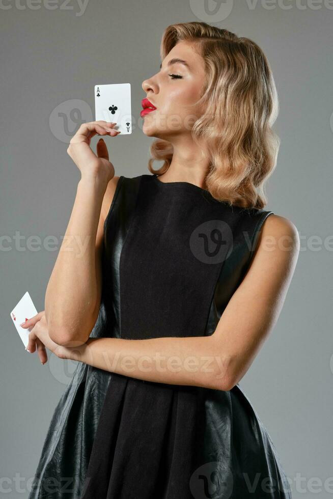 blond meisje in zwart elegant jurk tonen twee spelen kaarten, poseren tegen grijs achtergrond. het gokken amusement, poker, casino. detailopname. foto