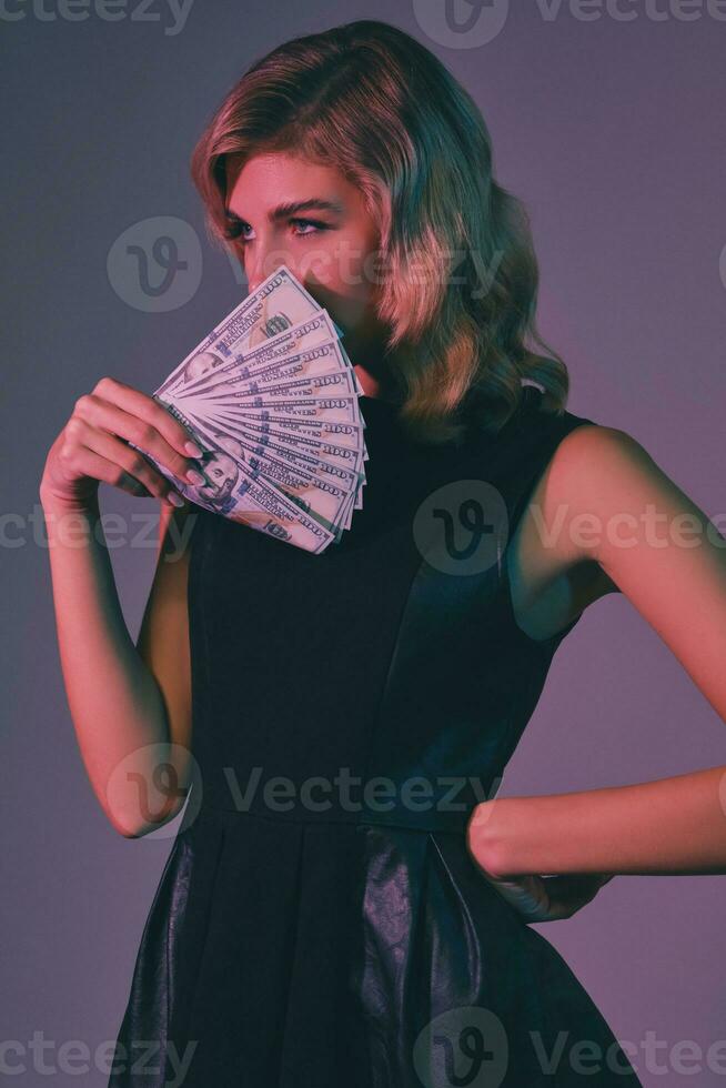 blond meisje in zwart elegant jurk Holding sommige geld, poseren tegen kleurrijk achtergrond. het gokken amusement, poker, casino. detailopname. foto