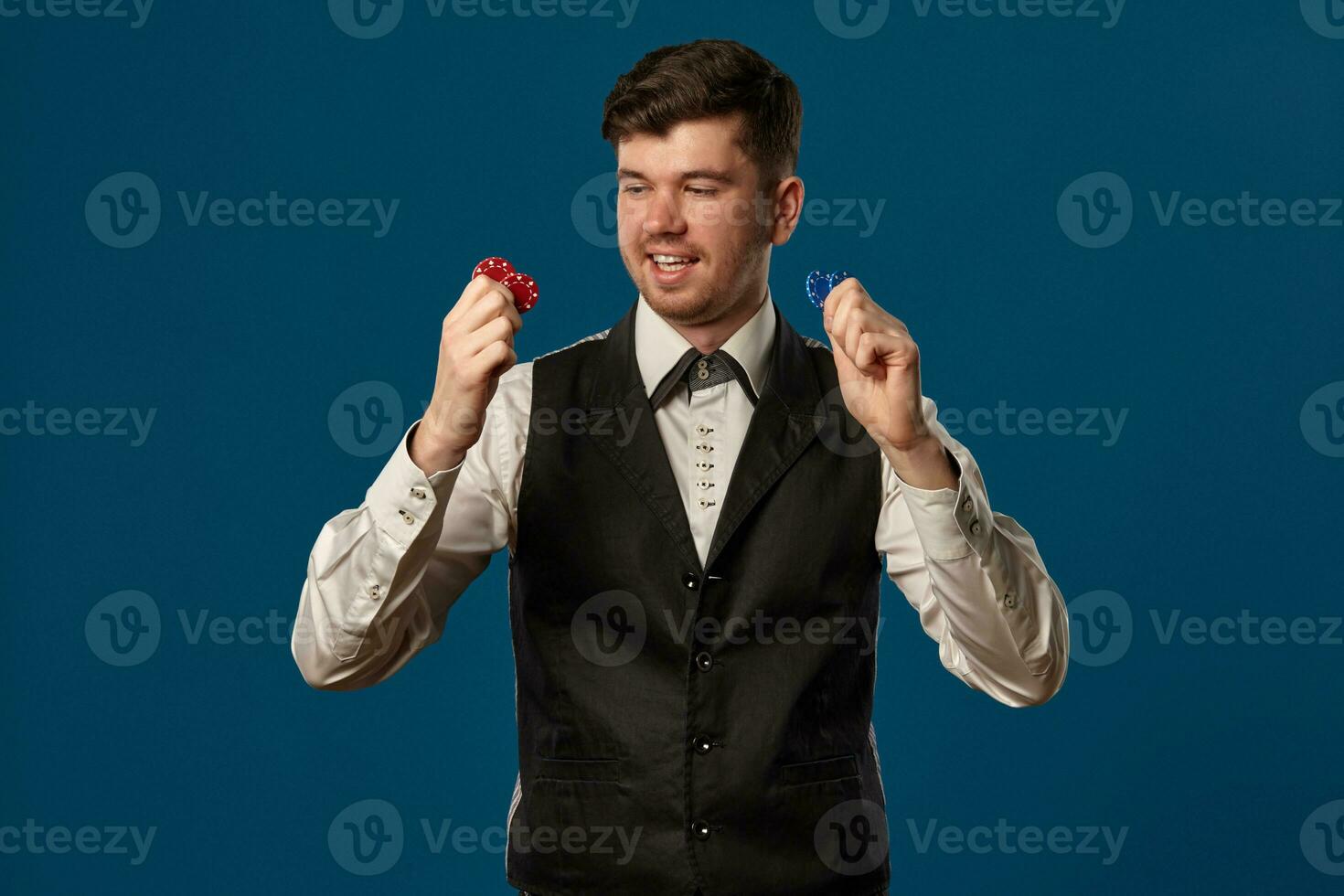 nieuweling in poker, in zwart hesje en wit shirt. Holding sommige gekleurde chips. poseren tegen blauw achtergrond. gokken, casino. detailopname. foto