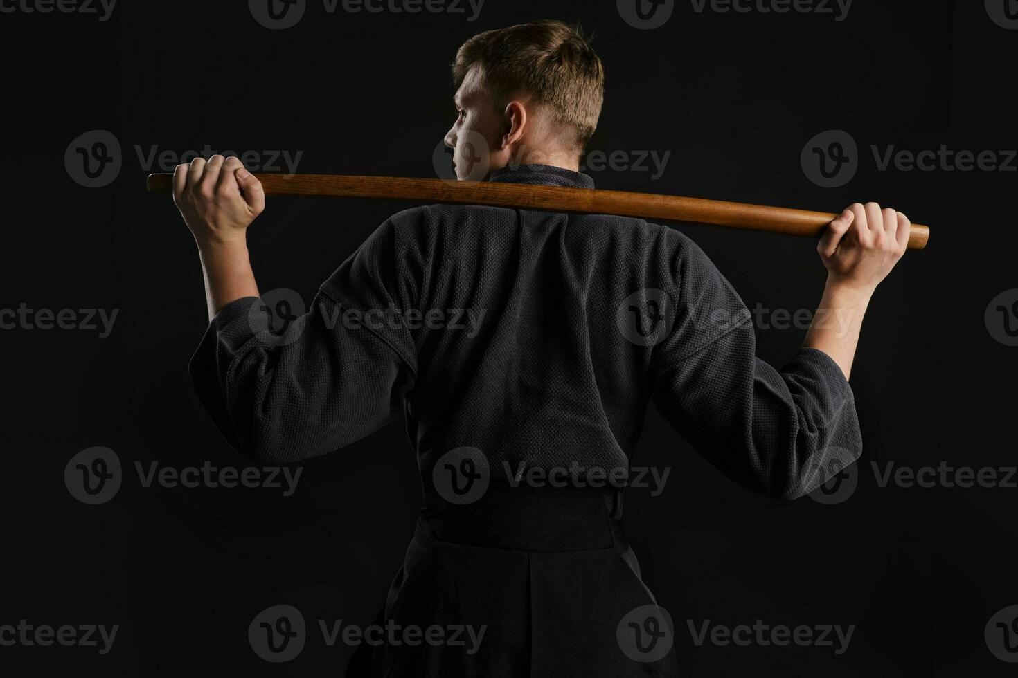 kendo goeroe vervelend in een traditioneel Japans kimono is beoefenen krijgshaftig kunst met de shinai bamboe zwaard tegen een zwart studio achtergrond. foto