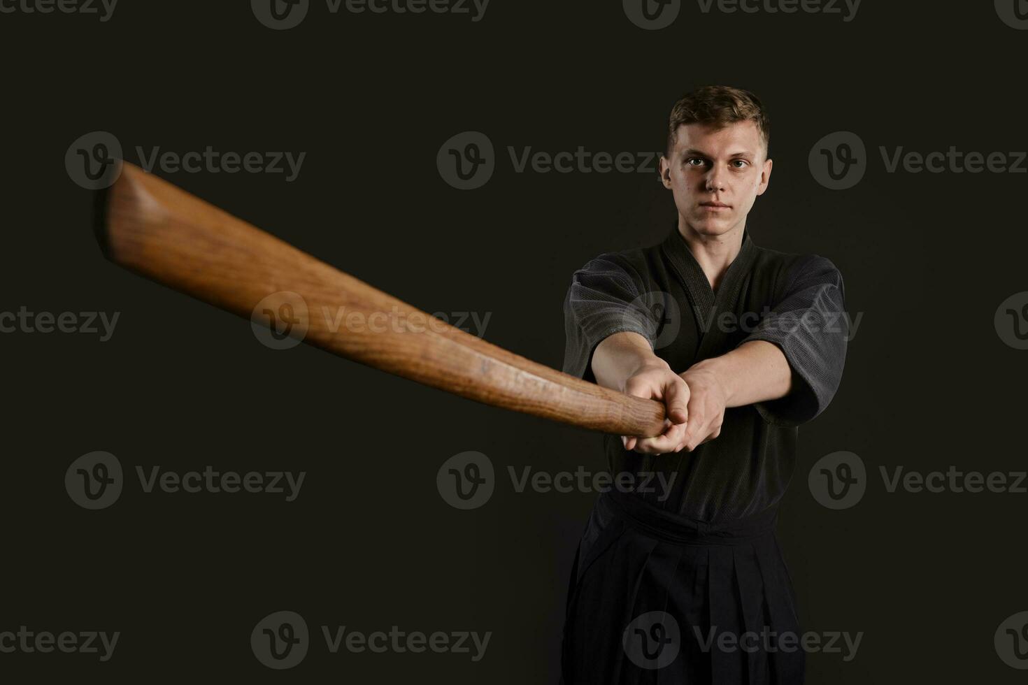 kendo goeroe vervelend in een traditioneel Japans kimono is beoefenen krijgshaftig kunst met de shinai bamboe zwaard tegen een zwart studio achtergrond. foto