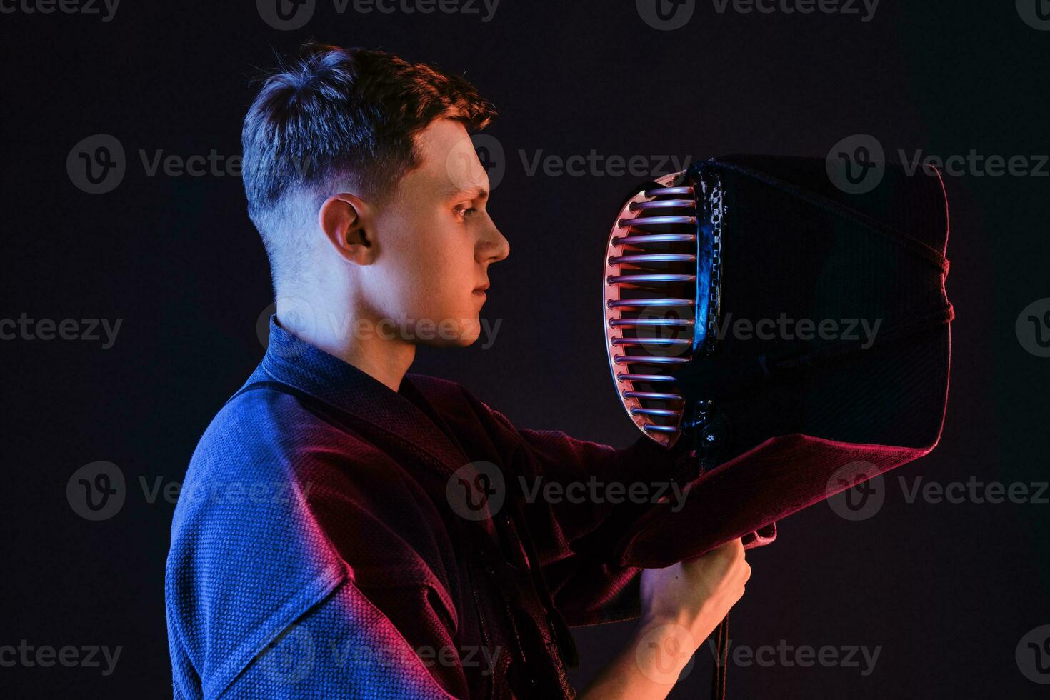 dichtbij omhoog schot, kendo vechter vervelend in een schild, traditioneel kimono is op zoek Bij zijn helm terwijl staand tegen een zwart studio achtergrond. foto