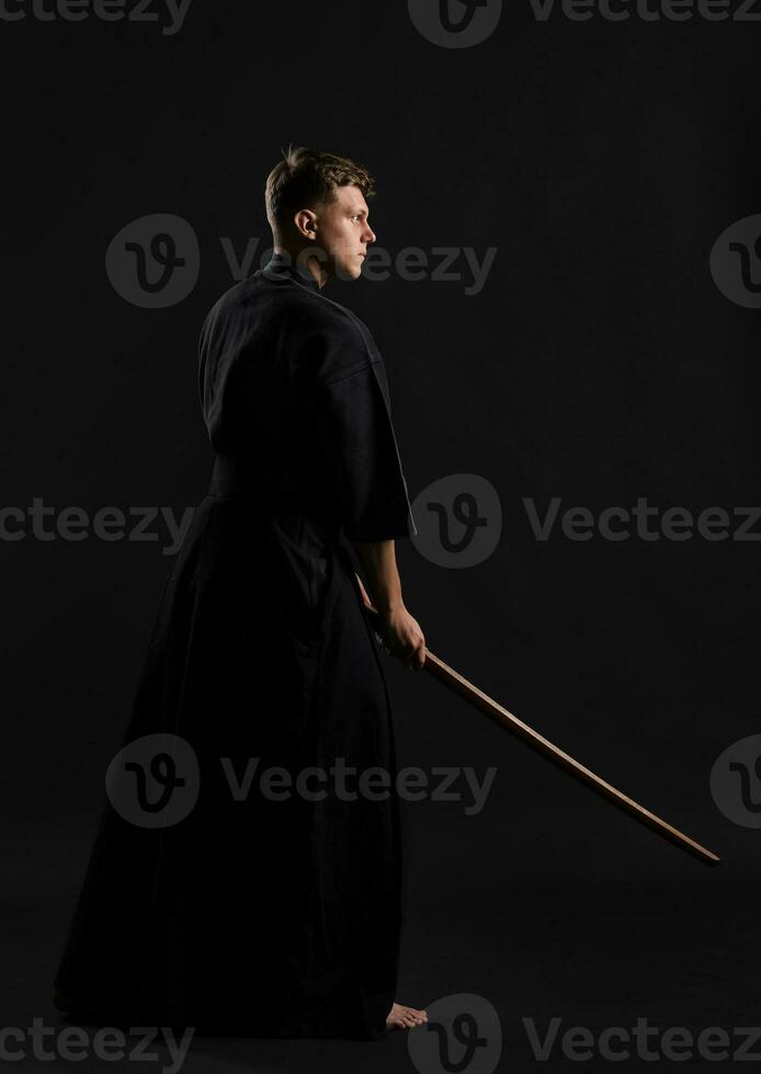 kendo goeroe vervelend in een traditioneel Japans kimono is beoefenen krijgshaftig kunst met de shinai bamboe zwaard tegen een zwart studio achtergrond. foto