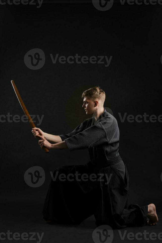 kendo goeroe vervelend in een traditioneel Japans kimono is beoefenen krijgshaftig kunst met de shinai bamboe zwaard tegen een zwart studio achtergrond. foto