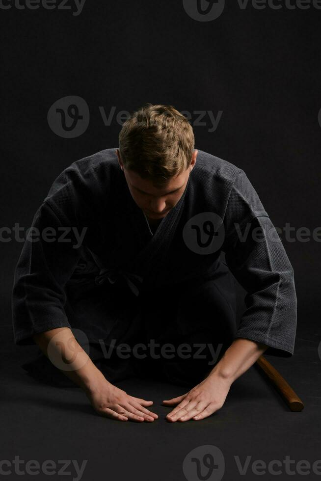 kendo goeroe vervelend in een traditioneel Japans kimono is beoefenen krijgshaftig kunst met de shinai bamboe zwaard tegen een zwart studio achtergrond. foto