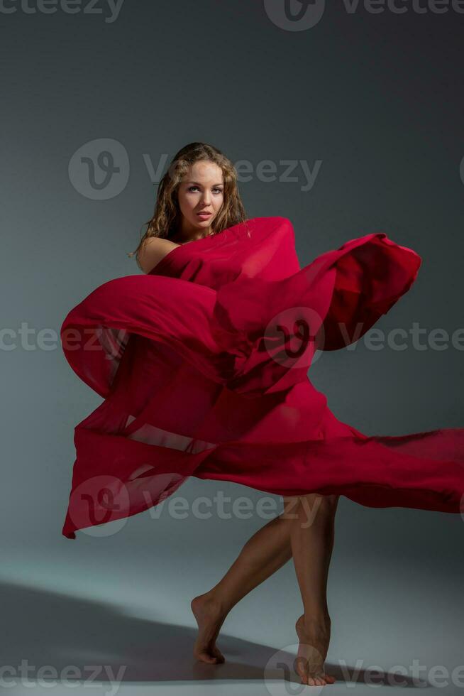 jong mooi danser in rood jurk poseren Aan een donker grijs studio achtergrond foto