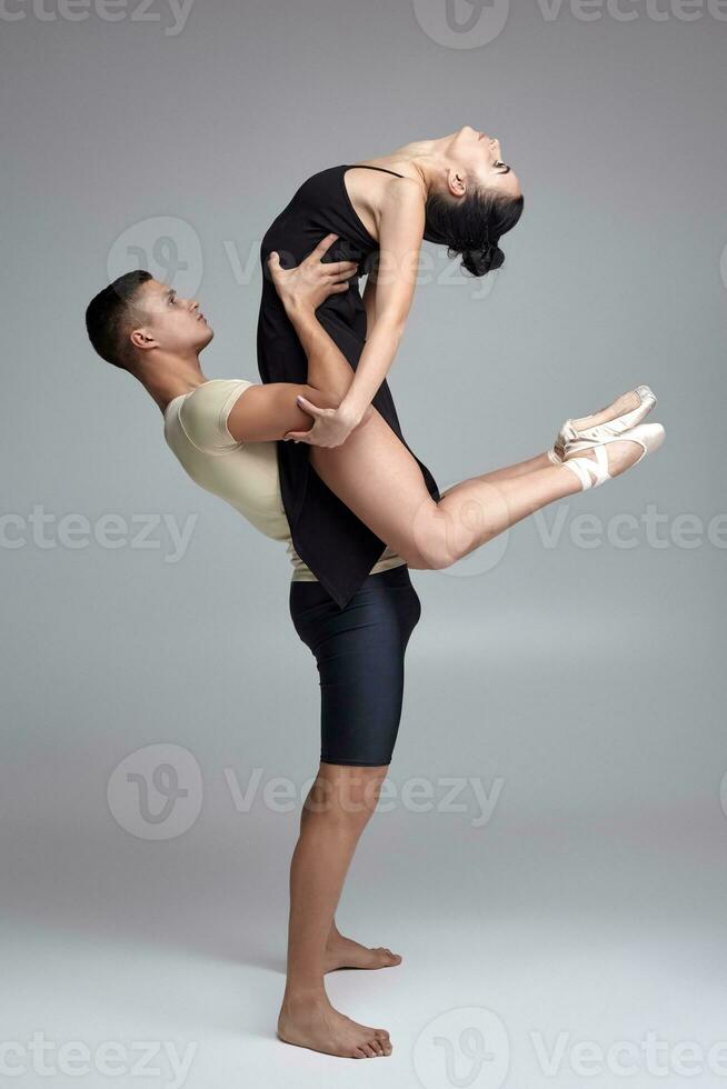 twee atletisch modern ballet dansers zijn poseren tegen een grijs studio achtergrond. foto