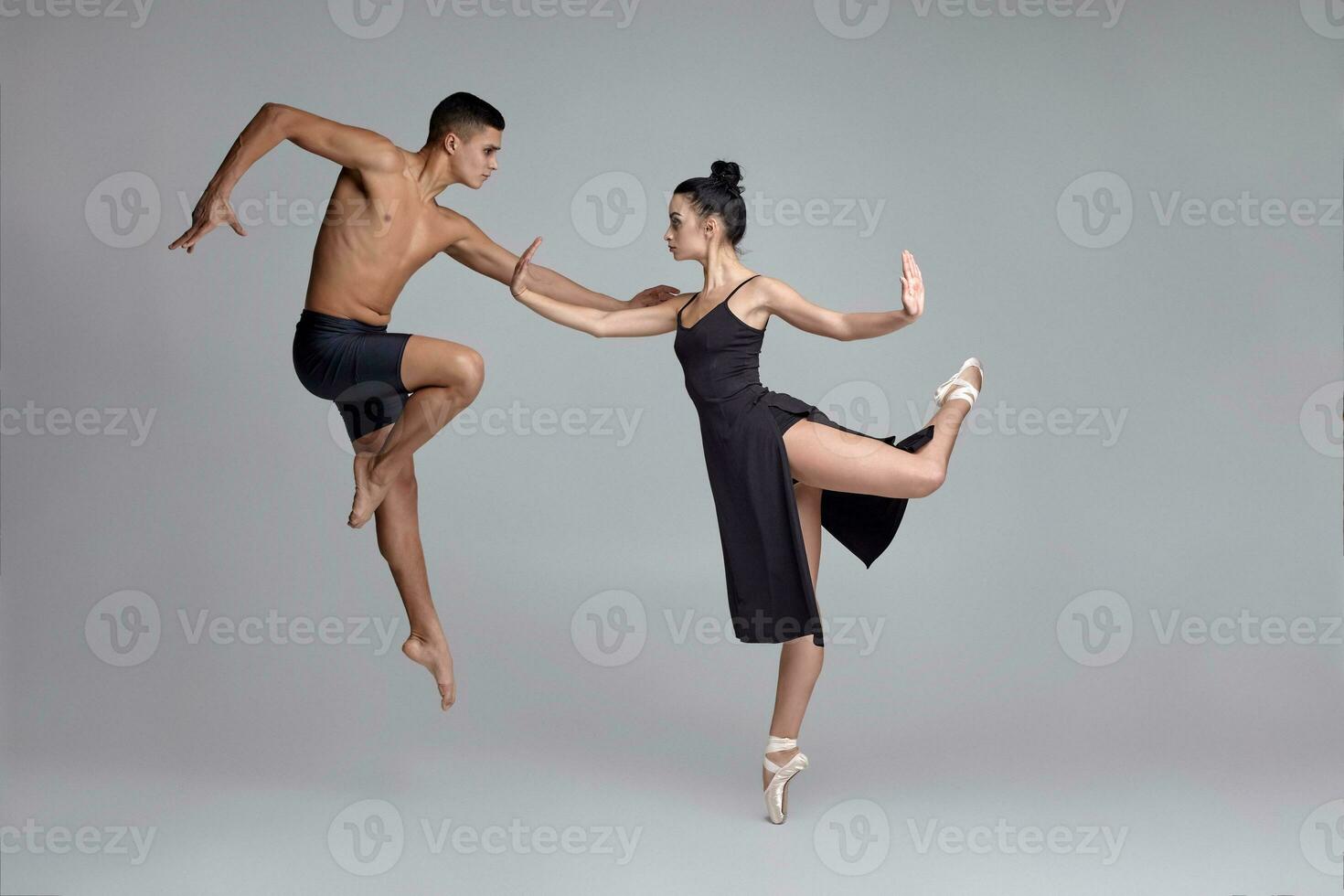 twee atletisch modern ballet dansers zijn poseren tegen een grijs studio achtergrond. foto