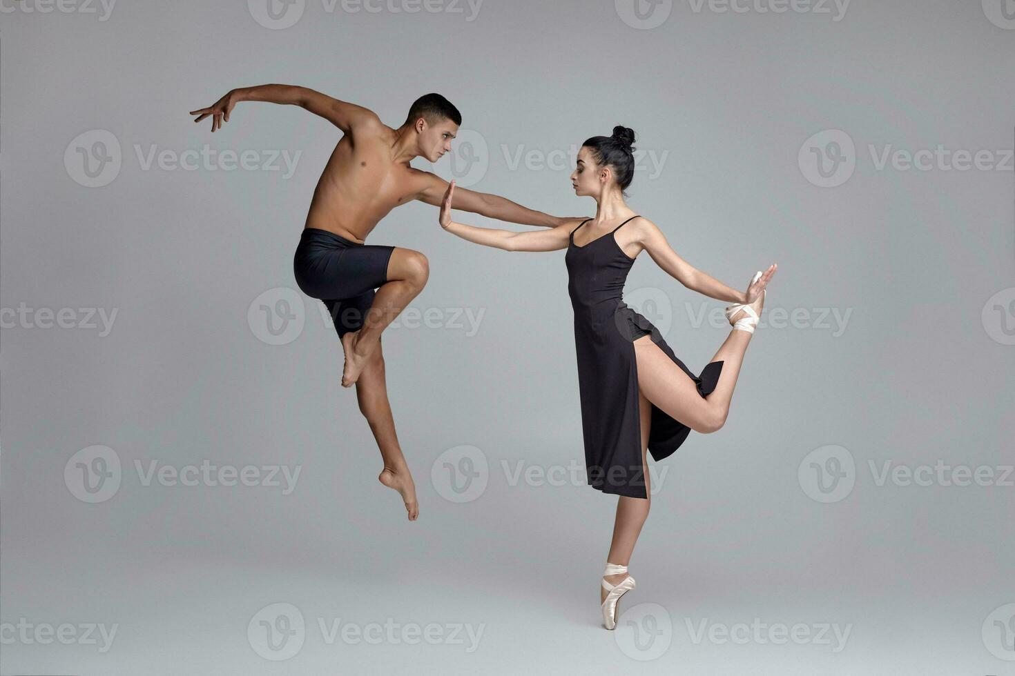 twee atletisch modern ballet dansers zijn poseren tegen een grijs studio achtergrond. foto