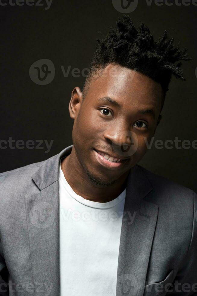 detailopname portret van knap zwart Mens met charmant glimlach. studio schot van goed gekleed Afrikaanse vent draagt wit t-shirt en grijs jasje. foto