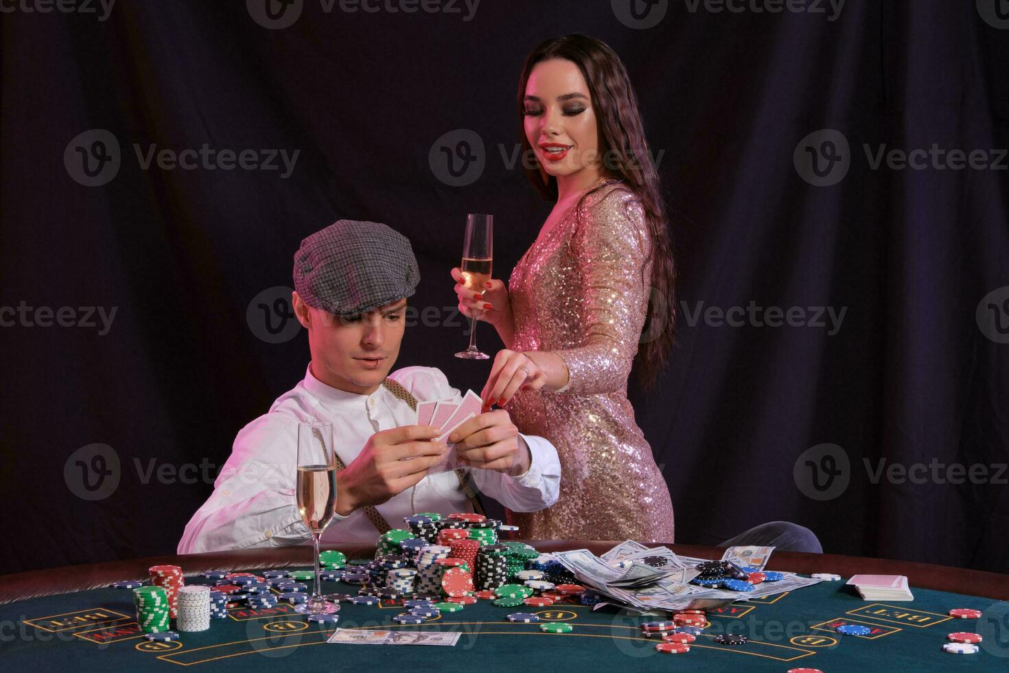 Mens spelen poker Bij casino zittend Bij tafel met stapels van chips, geld, Champagne, kaarten. vieren winnen met vrouw. zwart achtergrond. detailopname. foto